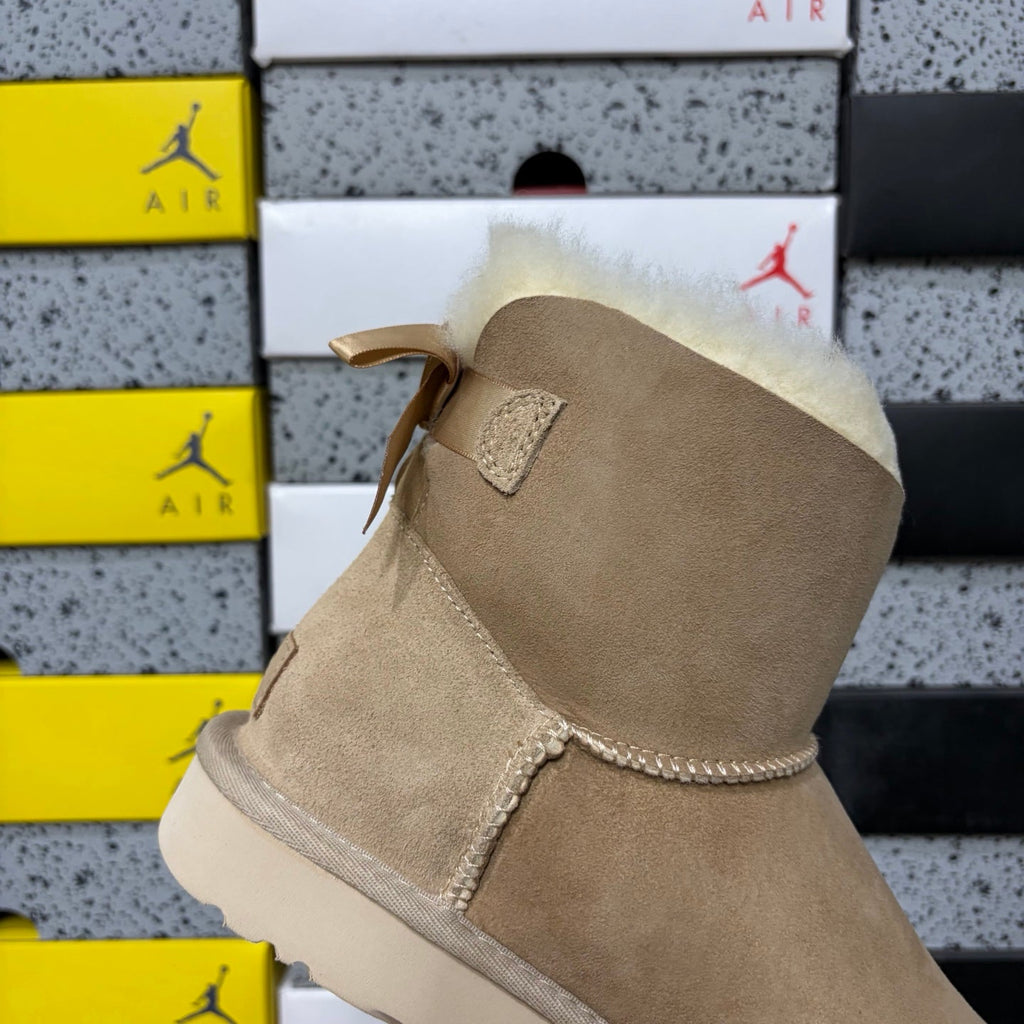 UGG Mini Bailey Bow Ankle Boot – Suede Boot with Cream Shearling Lining, Satin Bow Detail & Sand Sugar Sole in Sand